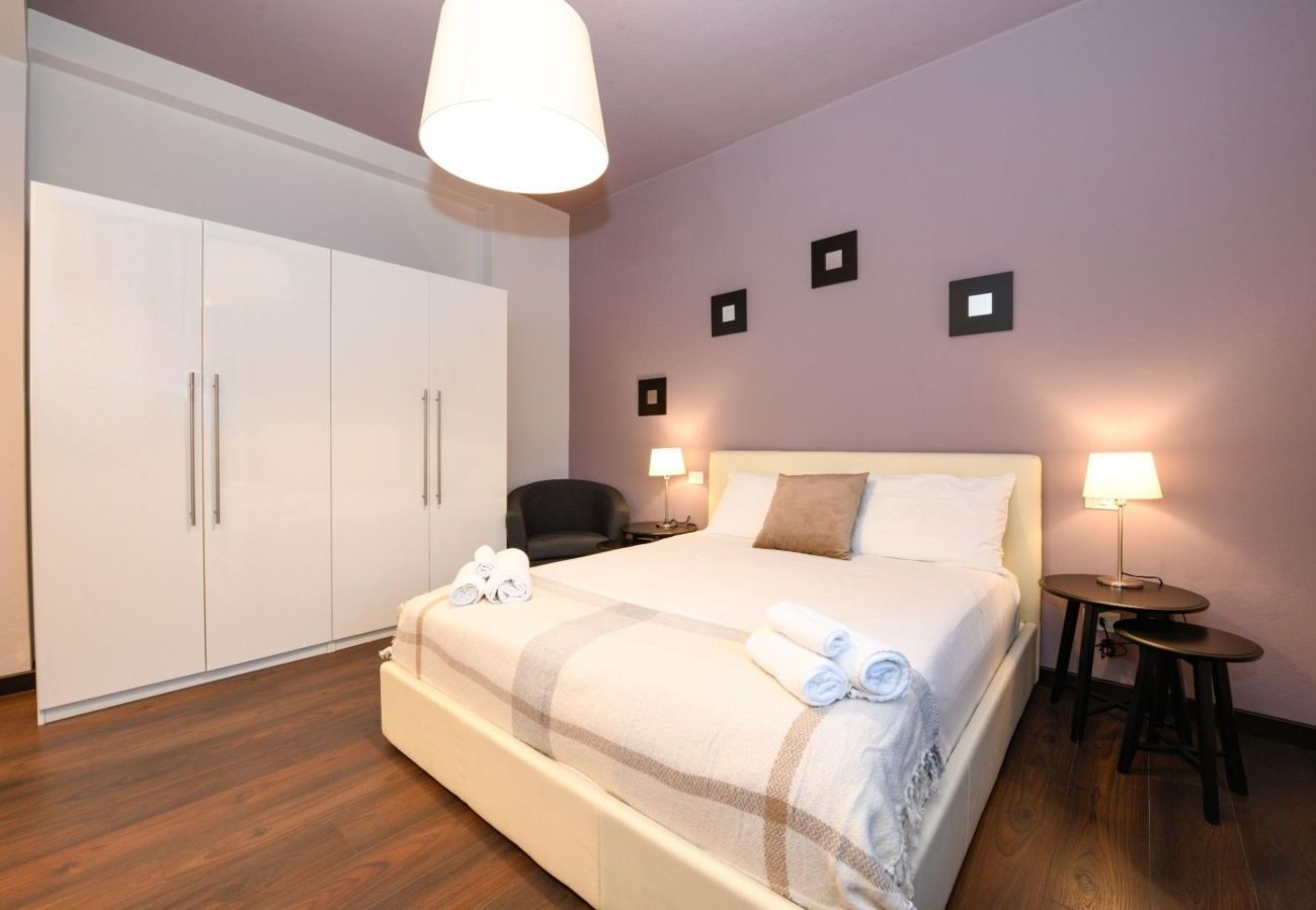 Nowoczesna sypialnia dwuosobowa z liliową ścianą, białą szafą i parkietem w Desenzano