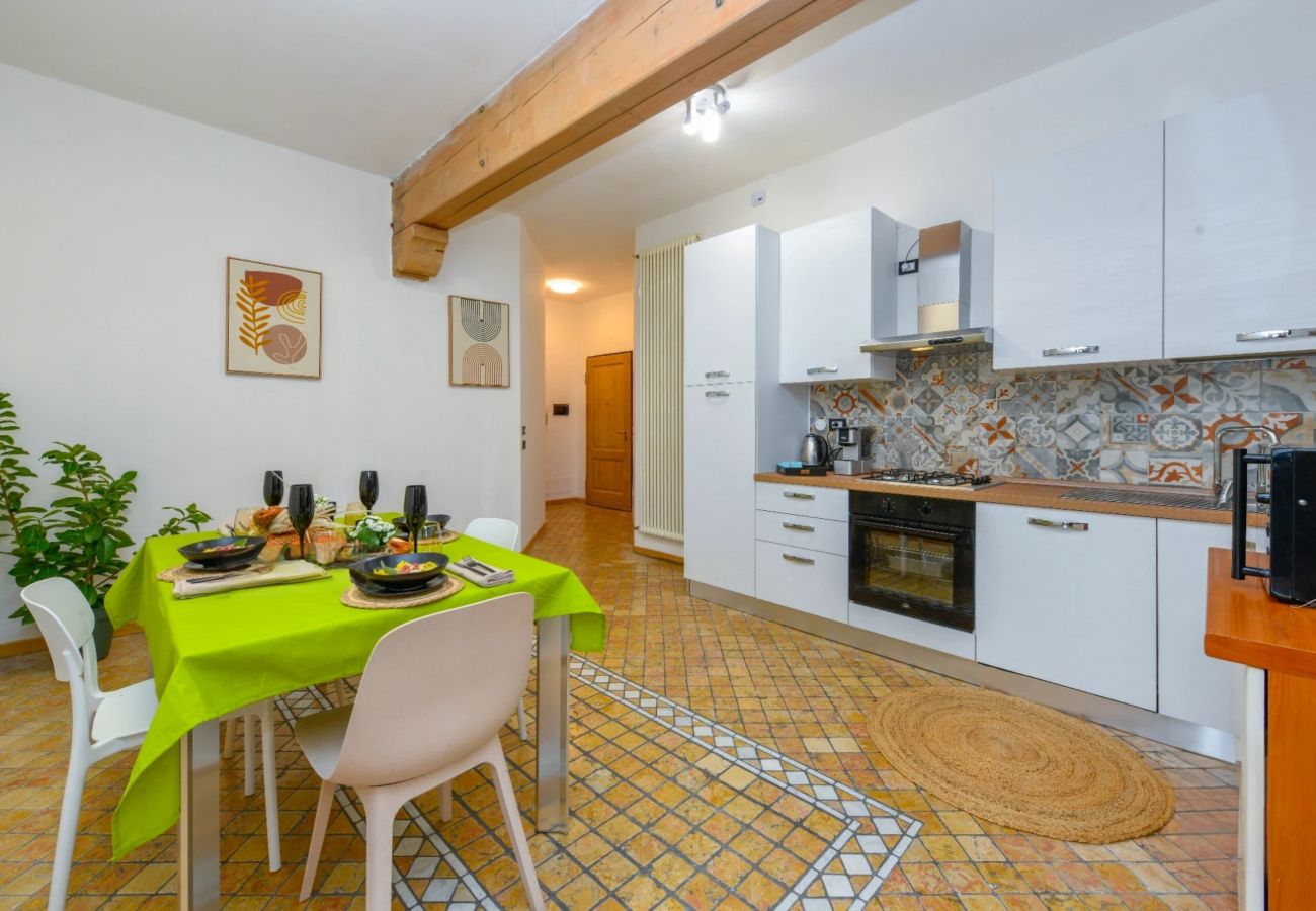 Biała kuchnia z dekoracyjnym panelem, stołem z zielonym obrusem i drewnianą belką w Desenzano